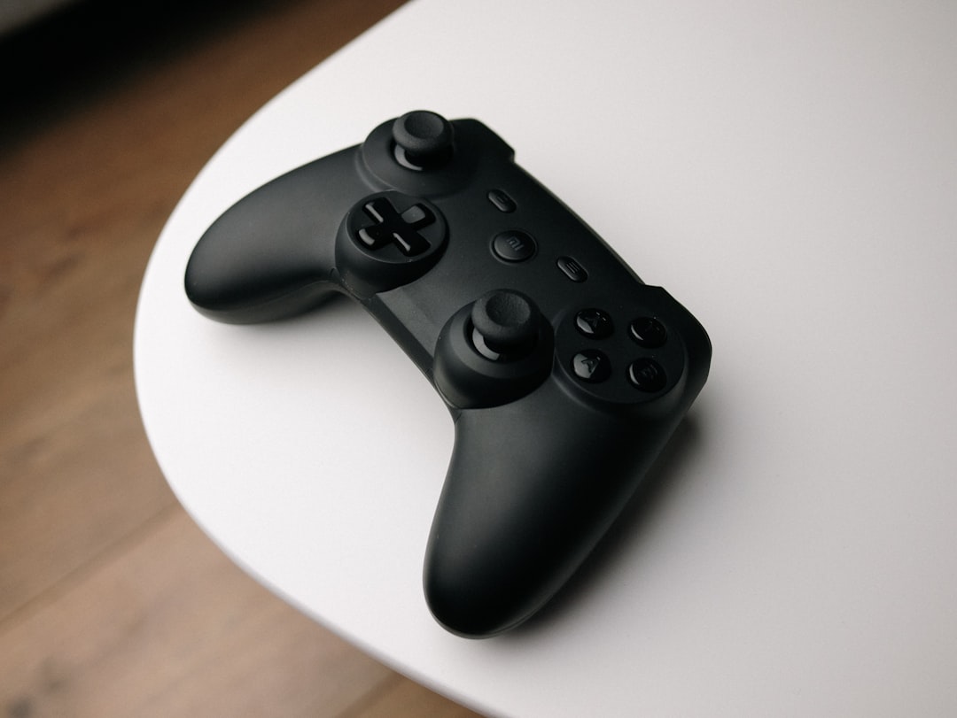 A matte-black gamepad resting on a small round side-table — the kind of quiet workspace used for bench-grading copies